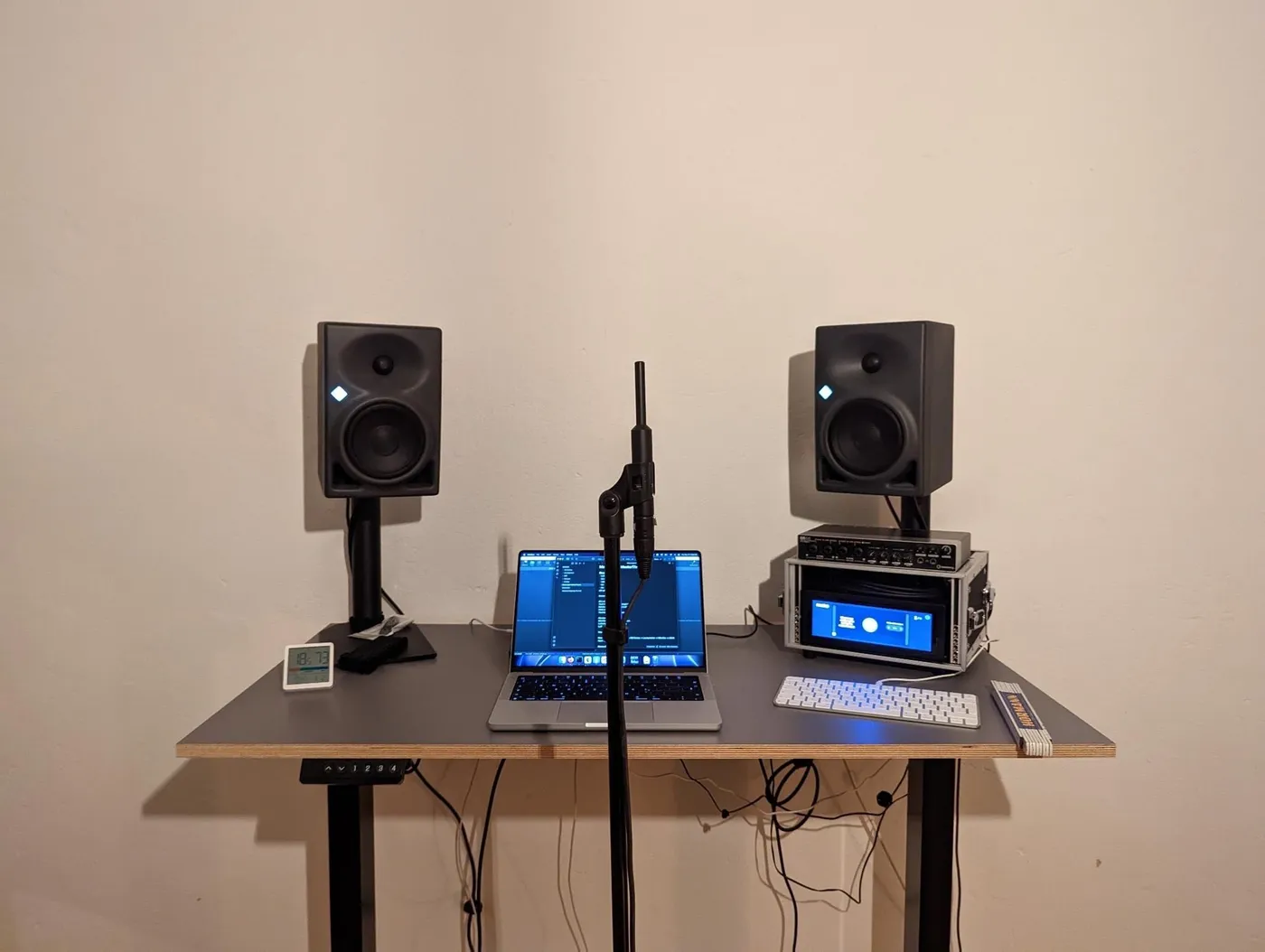 Two studio monitors on stands at a desk, a measurement microphone at the listening position, a laptop and the Studio Hub in a small rack case